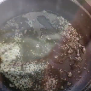 The image shows minced garlic in olive oil in a skillet