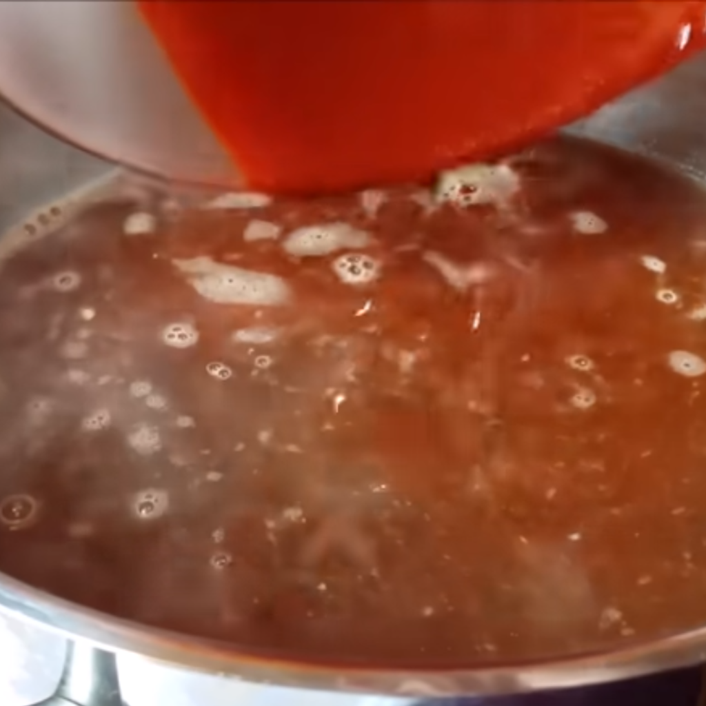 This image shows Adding chile puree and hominy to the pot for pozole